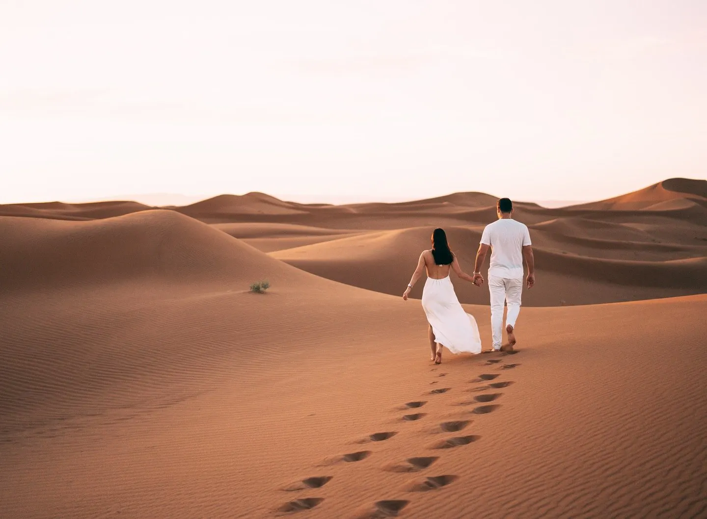 Couple walking across the Sahara dunes on a Morocco honeymoon